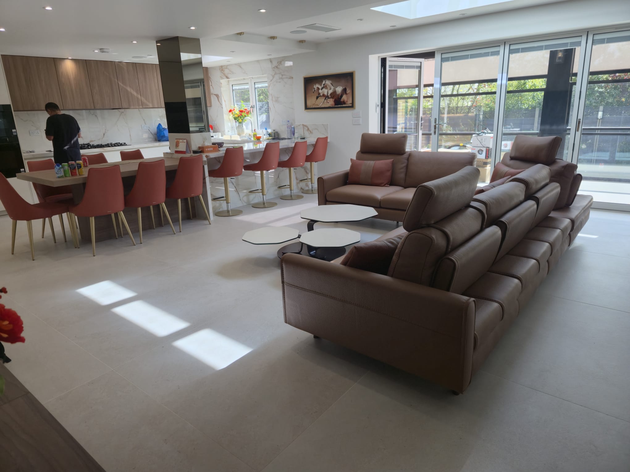 Open-plan kitchen and living space featuring matching terracotta dining chairs and bar stools with gold legs, complemented by tan leather sofas with coordinating cushions - FCI London client project